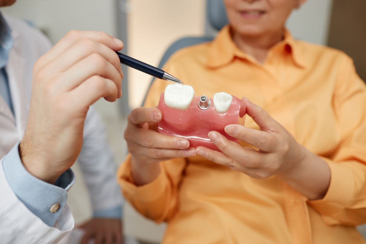 Dentist pointing to dental implant model showing bone structure and implant placement for patient education.