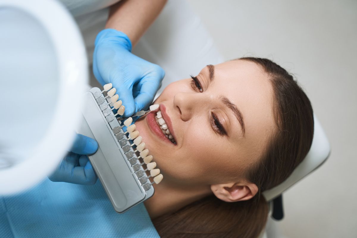 Dentist holding tooth shade guide next to patient's smile to determine whitening results.