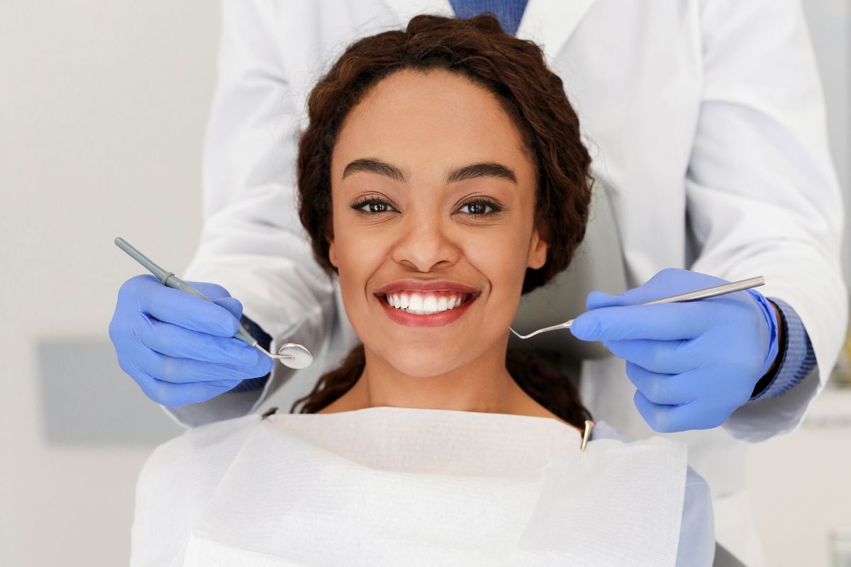 Smiling patient during professional dental examination with dentist holding examination tools.