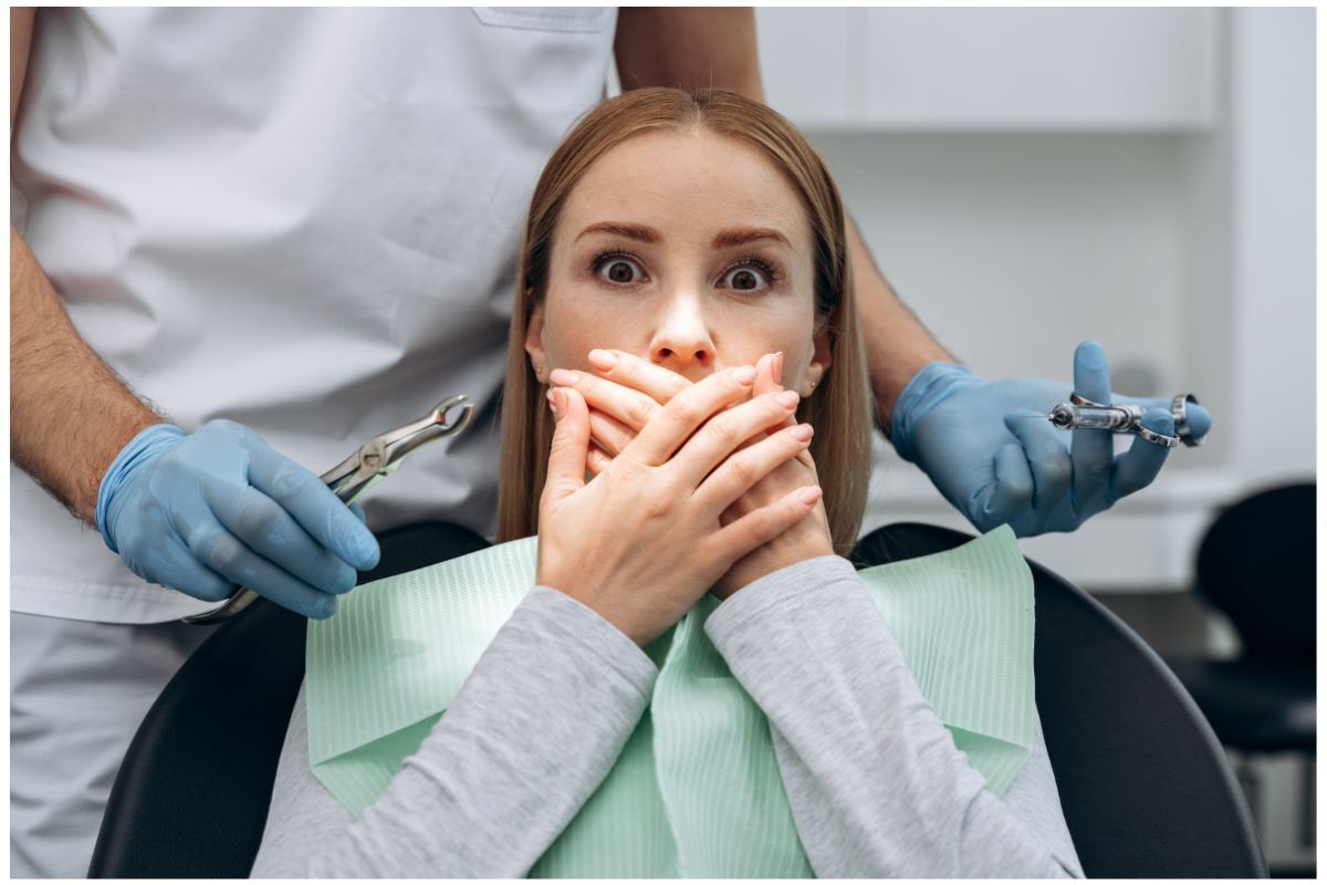 Anxious patient covering mouth while dentist holds dental instruments during root canal consultation.