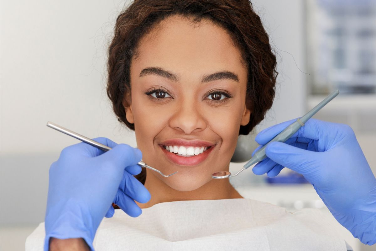 Smiling patient showing healthy teeth during dental examination with dentist tools.
